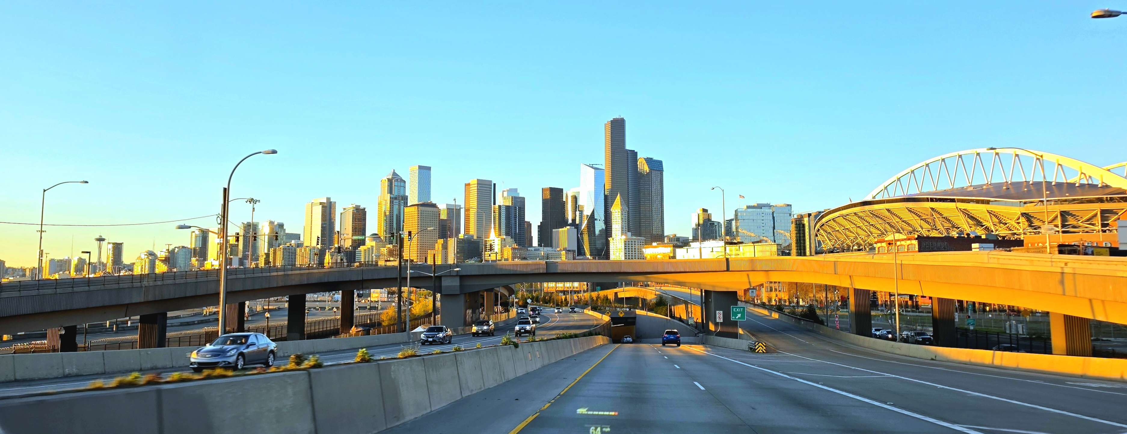 The Seattle skyline at golden hour, seen from a highway overpass with the Space Needle on the horizon